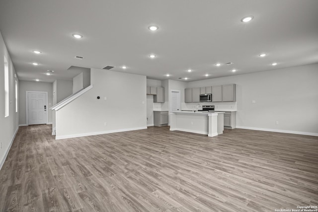 unfurnished living room with wood finished floors, baseboards, and recessed lighting