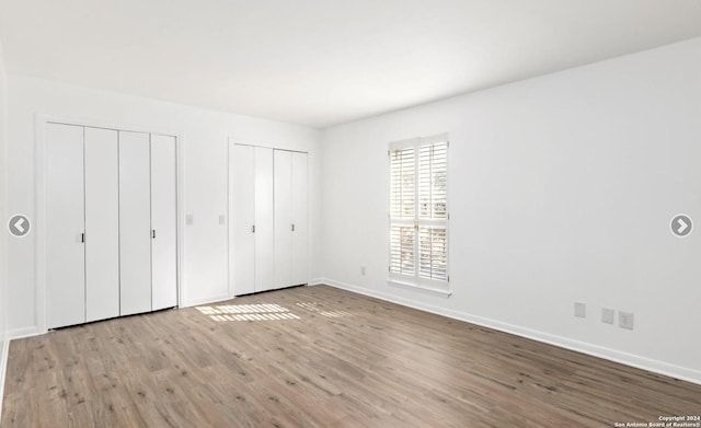 unfurnished bedroom with multiple closets, baseboards, and light wood finished floors