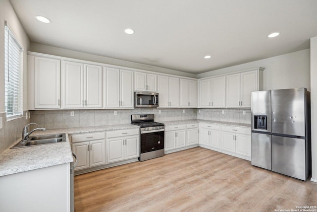 kitchen featuring light countertops, appliances with stainless steel finishes, white cabinets, a sink, and light wood-type flooring