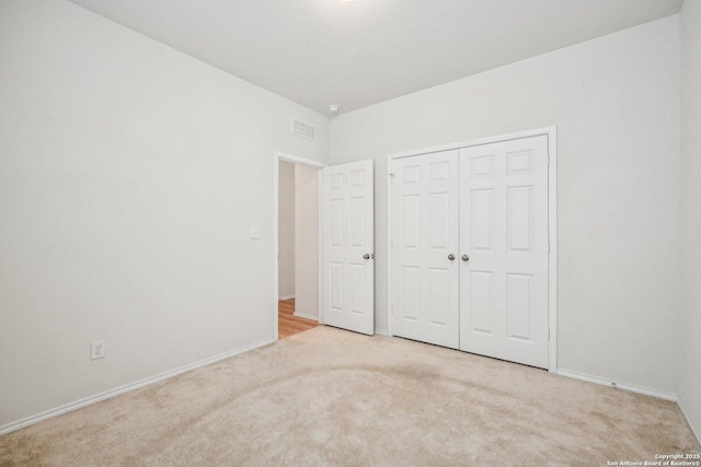 unfurnished bedroom with light carpet, a closet, visible vents, and baseboards