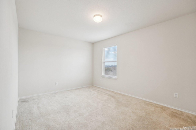 spare room with baseboards and light colored carpet