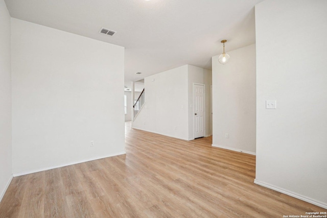 unfurnished room featuring stairway, visible vents, light wood-style flooring, and baseboards