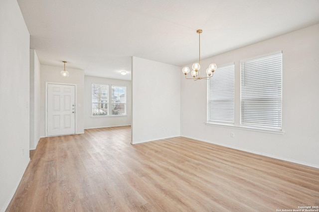 spare room with baseboards, light wood-style flooring, and a notable chandelier