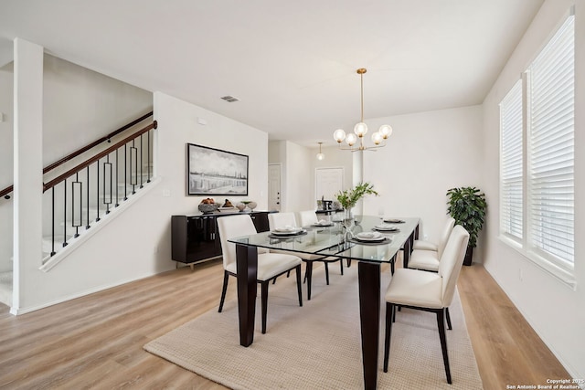 dining area with light wood finished floors, stairs, visible vents, and a notable chandelier