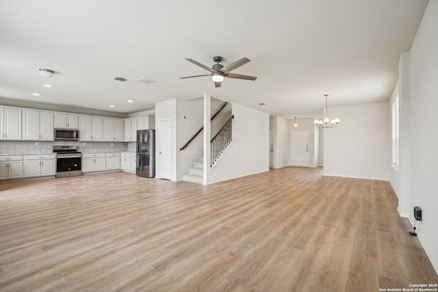 unfurnished living room with ceiling fan with notable chandelier, stairway, light wood-type flooring, and visible vents