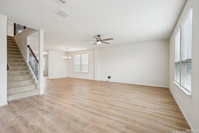 unfurnished living room featuring light wood-style floors, ceiling fan with notable chandelier, baseboards, and stairs