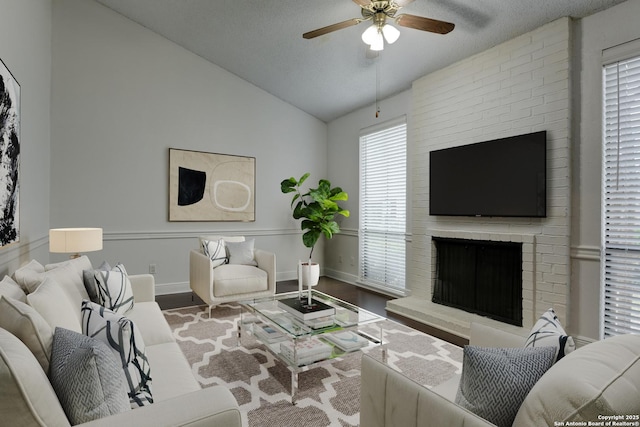 living area featuring lofted ceiling, ceiling fan, wood finished floors, baseboards, and a brick fireplace