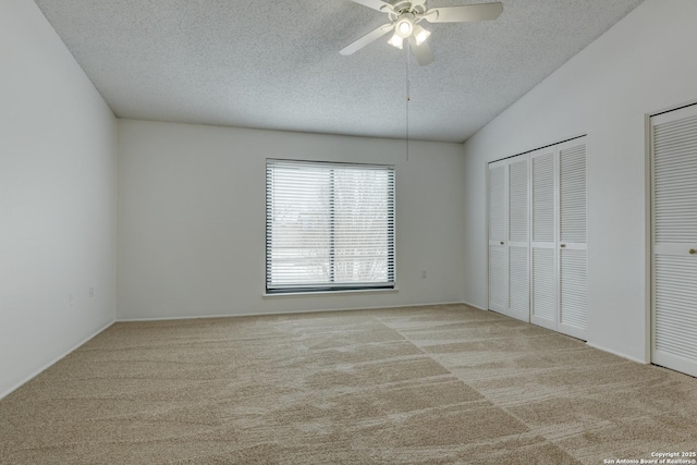 unfurnished bedroom with multiple closets, vaulted ceiling, carpet floors, and a textured ceiling