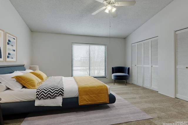 carpeted bedroom featuring lofted ceiling, ceiling fan, a textured ceiling, and multiple closets