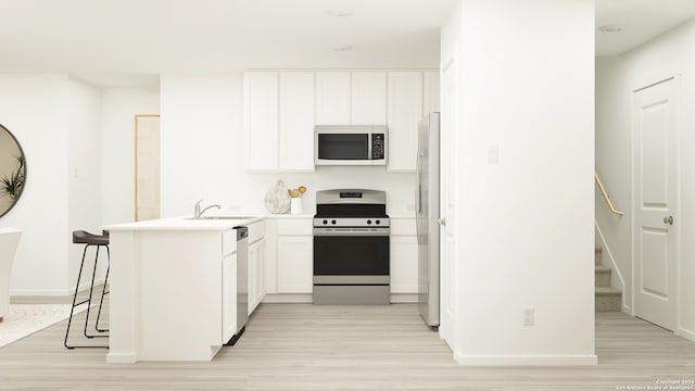 kitchen featuring a peninsula, stainless steel appliances, a sink, white cabinetry, and light countertops