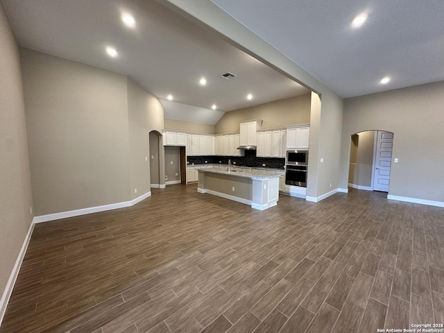 kitchen featuring arched walkways, a center island with sink, visible vents, open floor plan, and white cabinetry