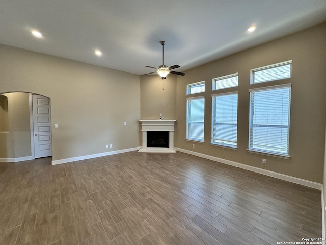 unfurnished living room featuring arched walkways, a fireplace with raised hearth, wood finished floors, and baseboards