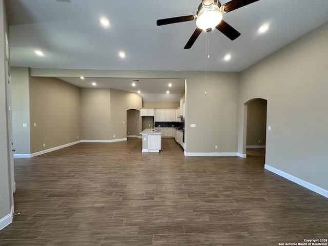 unfurnished living room with arched walkways, dark wood-style flooring, recessed lighting, a ceiling fan, and baseboards