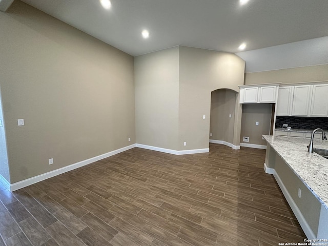 kitchen with arched walkways, light stone countertops, wood tiled floor, white cabinetry, and a sink