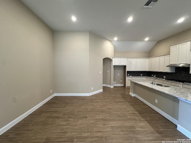 kitchen with light stone counters, arched walkways, black stovetop, white cabinetry, and a sink