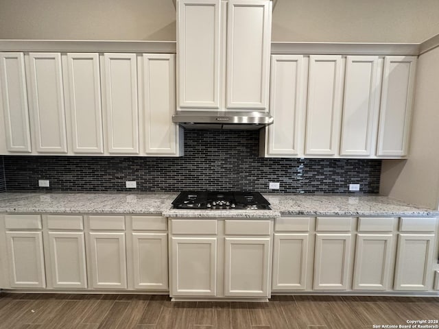 kitchen with light stone counters, tasteful backsplash, stainless steel gas stovetop, white cabinets, and under cabinet range hood