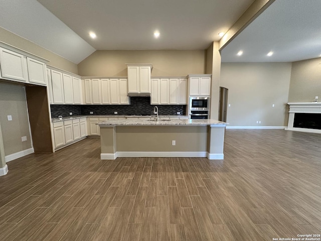 kitchen with stainless steel appliances, white cabinetry, an island with sink, and light stone countertops