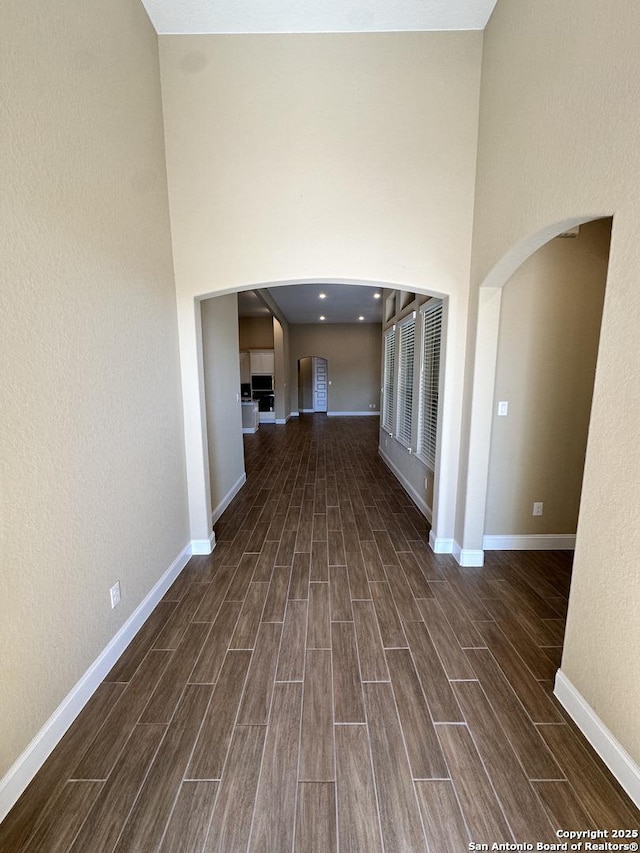 interior space with a towering ceiling, wood finish floors, arched walkways, and baseboards