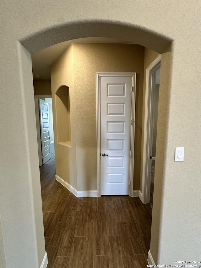 hallway with wood tiled floor, arched walkways, and baseboards