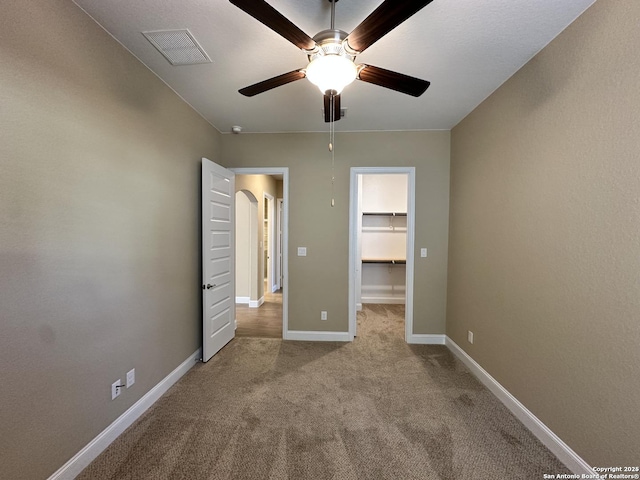 unfurnished bedroom with light carpet, baseboards, visible vents, a ceiling fan, and a walk in closet