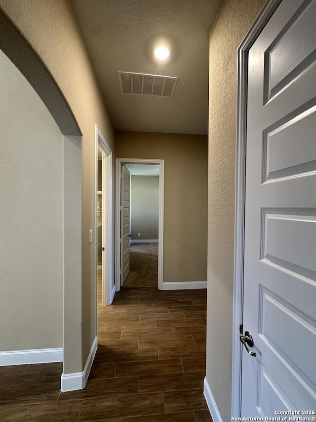 hall with baseboards, a textured ceiling, visible vents, and wood tiled floor