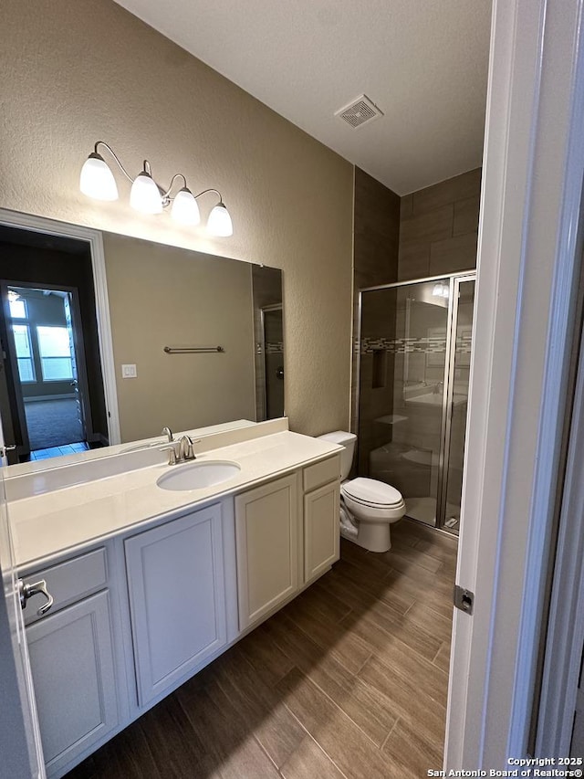 full bath with a stall shower, visible vents, a textured wall, toilet, and wood finished floors