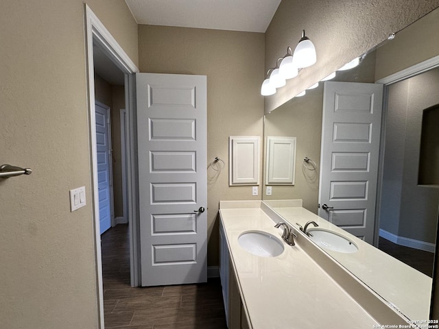 bathroom with a textured wall, vanity, baseboards, and wood finished floors