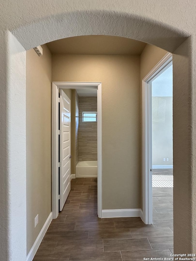 corridor featuring arched walkways, baseboards, and wood tiled floor