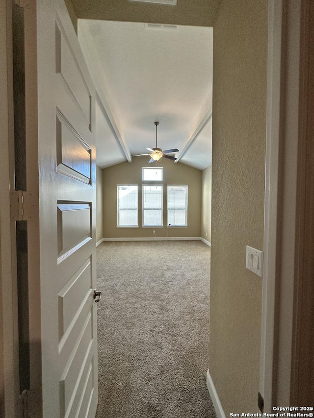 empty room with baseboards, a ceiling fan, a textured wall, light colored carpet, and vaulted ceiling