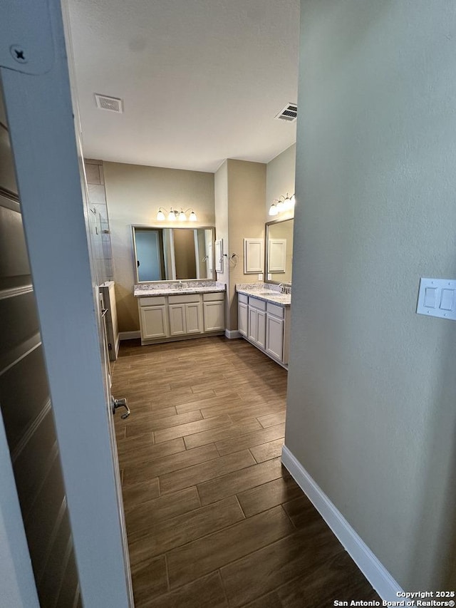 bathroom featuring two vanities, wood tiled floor, visible vents, and baseboards