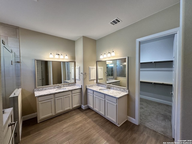 full bath with wood finished floors, two vanities, a sink, visible vents, and a spacious closet