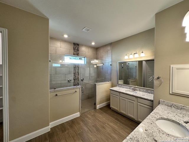 full bathroom featuring wood finished floors, a stall shower, two vanities, and a sink