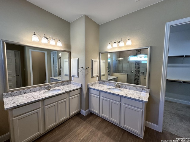 bathroom with a stall shower, wood finished floors, a sink, a spacious closet, and two vanities