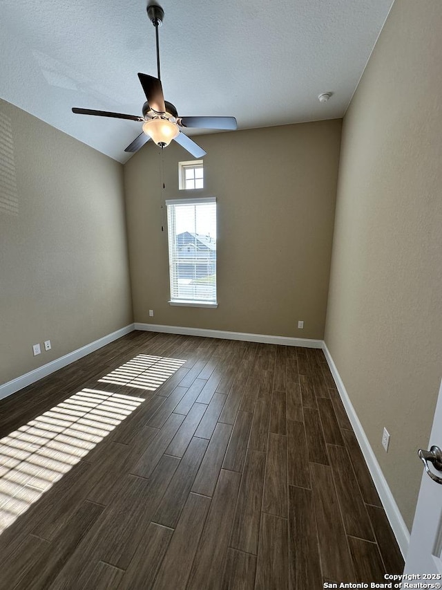 spare room featuring baseboards, dark wood finished floors, a ceiling fan, vaulted ceiling, and a textured ceiling