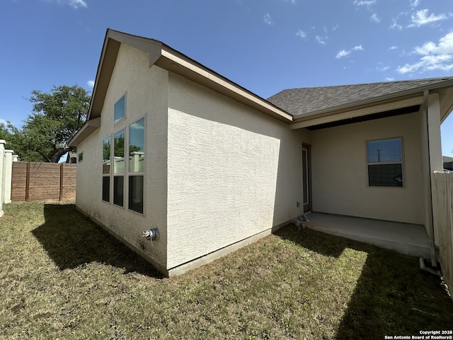 view of side of property featuring fence, a yard, roof with shingles, stucco siding, and a patio area