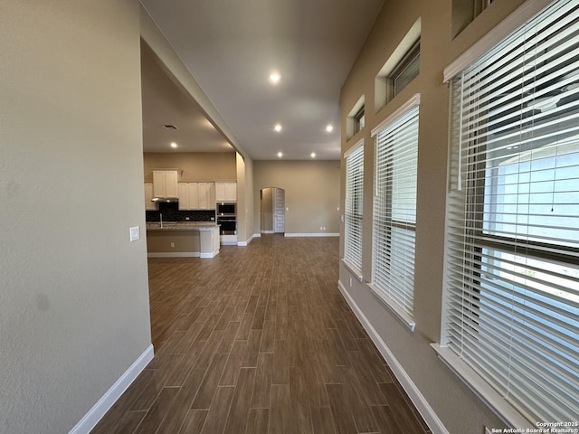 hall featuring arched walkways, recessed lighting, a sink, baseboards, and dark wood-style floors