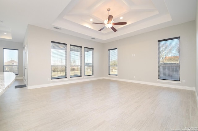 spare room with a tray ceiling, visible vents, and baseboards