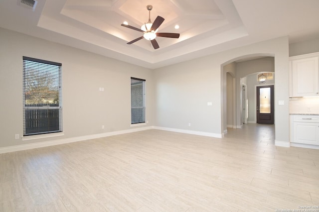 empty room featuring arched walkways, a raised ceiling, visible vents, and light wood finished floors