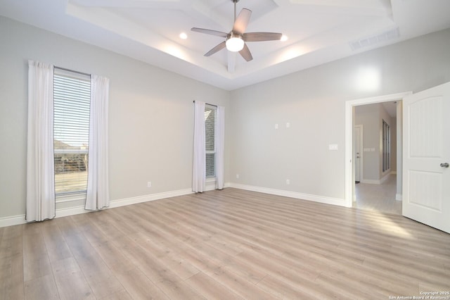 empty room with a wealth of natural light, light wood-style flooring, a raised ceiling, and visible vents