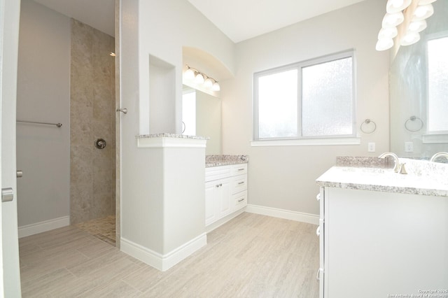 bathroom with a walk in shower, wood finished floors, two vanities, a sink, and baseboards