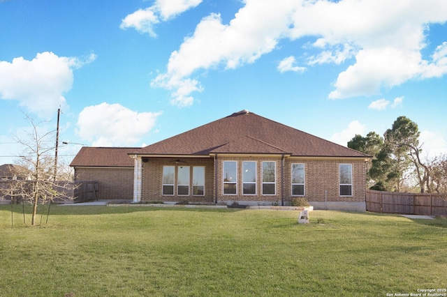 rear view of house featuring a yard, brick siding, and fence