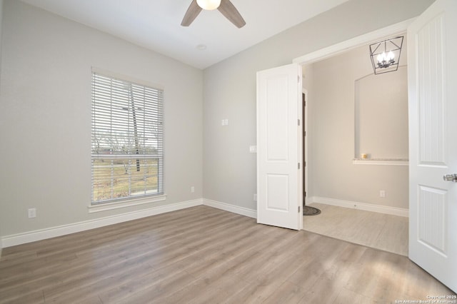 unfurnished room featuring ceiling fan with notable chandelier, baseboards, and wood finished floors