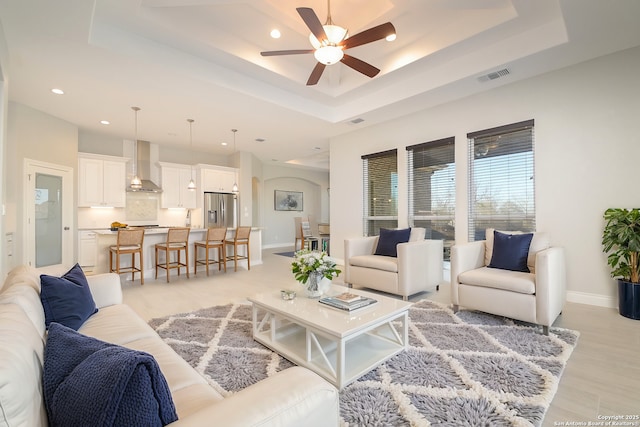 living area featuring a tray ceiling, visible vents, ceiling fan, and baseboards