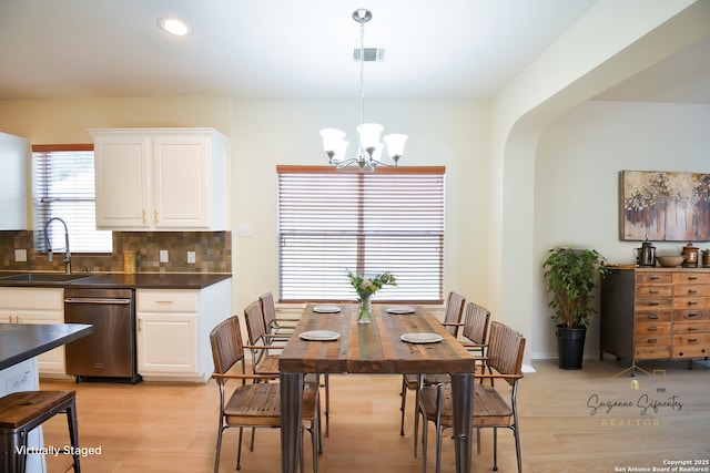 dining space with arched walkways, recessed lighting, a notable chandelier, visible vents, and light wood-type flooring