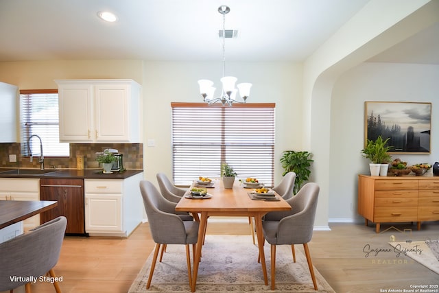 dining area featuring baseboards, visible vents, light wood finished floors, and an inviting chandelier