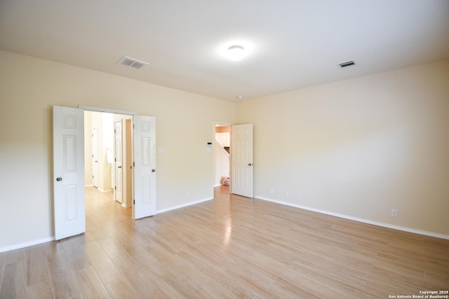 spare room featuring light wood-type flooring, visible vents, and baseboards