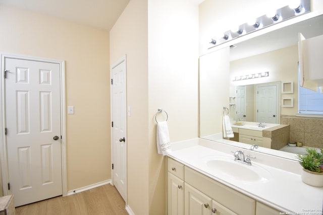 bathroom featuring a tub to relax in, two vanities, a sink, and wood finished floors