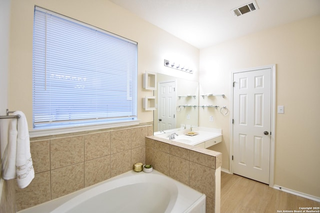 full bath with a garden tub, wood finished floors, vanity, visible vents, and baseboards