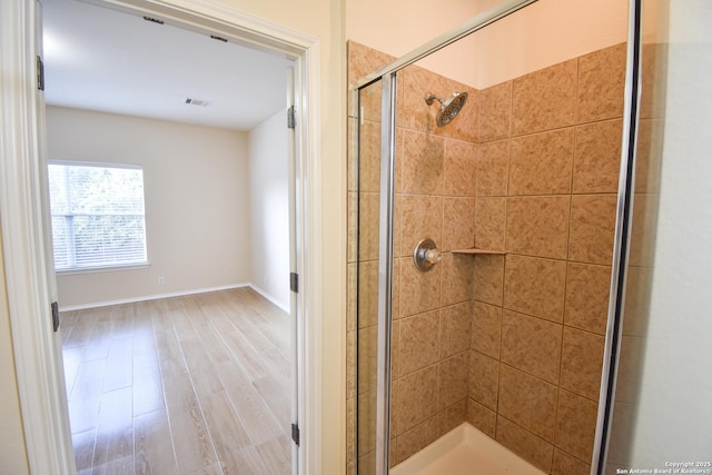 full bathroom featuring tiled shower, wood finished floors, visible vents, and baseboards