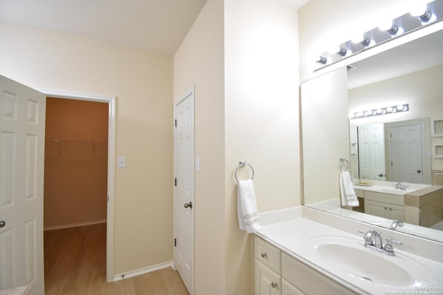 bathroom with baseboards, wood finished floors, a sink, a walk in closet, and two vanities